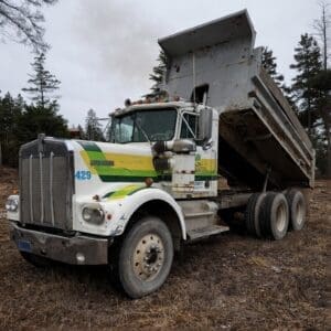 White heavy-duty dump truck with a raised bed in a dirt lot, green and yellow stripes along the side.