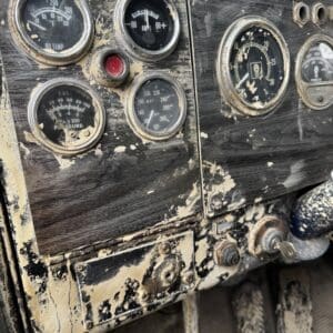 Old dusty vehicle dashboard with worn gauges and a red warning light, mud splattered across panels.