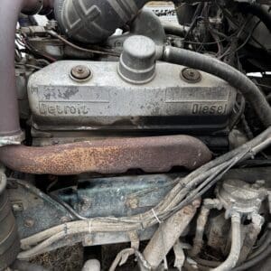 Dusty Detroit Diesel engine block with a rusted exhaust pipe and tangled hoses in an old vehicle bay