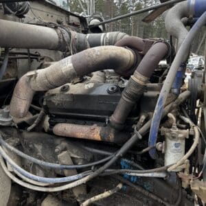 Close-up of a dusty diesel truck engine with a rusty exhaust manifold and tangled hoses in an outdoor engine bay.