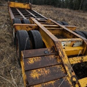 Rusty yellow heavy-duty trailer frame with multiple worn tires in a dry grassy field.