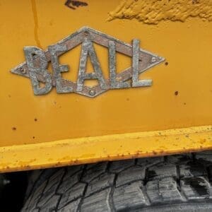 Metal BEALL logo on a yellow industrial vehicle with a large treaded tire visible below.