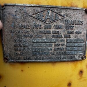 Metal nameplate on a yellow background from Beall Trailers, listing company name and technical specs (model, capacity, serial number).