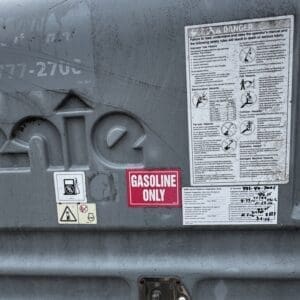 Close-up of a gray fuel tanker with a red 'Gasoline Only' sticker and multiple warning labels, outdoors.