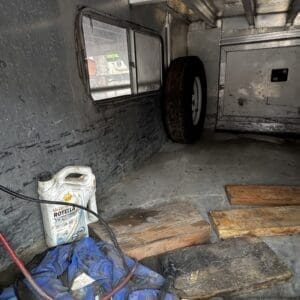 Interior of a utility trailer with a spare tire, oil jug, blue bag, and wooden planks on the floor.