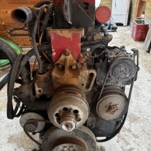 Rusty, weathered automotive engine with belts and pulleys in a wooden workshop, sitting on a wooden block.