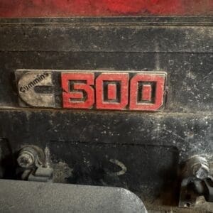 Close-up of a dusty Cummins engine badge reading '500' on a dark engine block.