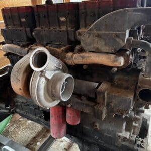 Diesel engine mounted on a frame, showing a prominent turbocharger and rusty intake pipes.
