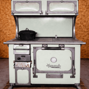 Vintage green Monarch kitchen stove with metal trim, a black pot on the left burner, set against a wooden pallet background in a workshop.