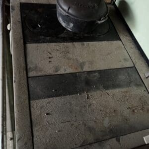 Dusty old metal stove with a round cast-iron kettle on top, in a cluttered workshop.