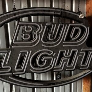 Neon Bud Light sign hung with chains in a workshop or garage setting