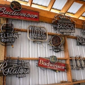 Collection of vintage neon beer signs mounted on a wooden-framed corrugated metal wall surface.