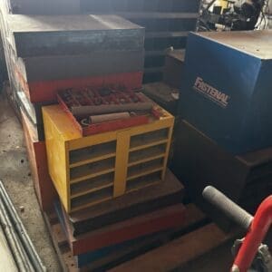 Industrial workshop scene with a yellow divided tool organizer on wooden pallets and a blue Fastenal cabinet nearby.