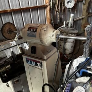 Jet bench grinder on a stand in a cluttered workshop; grinding wheel on the left and a guard in place.