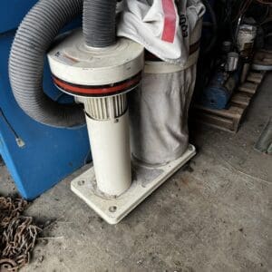 Dust extraction unit with a large corrugated hose, bolted to a base, in a cluttered workshop corner.