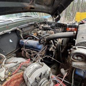 Old truck engine bay with rusted components, exposed wires, and a dusty alternator in a cluttered layout.