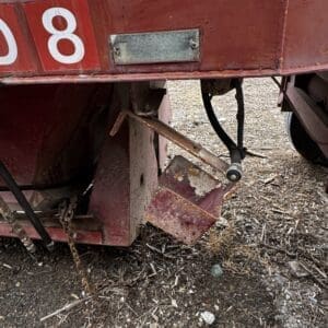 Rear underside of a red trailer, with rusted metal supports, a bent step, and hanging chain near the ground.