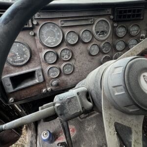 Interior of a dusty truck cab showing a worn steering wheel, gauges, and control panel.