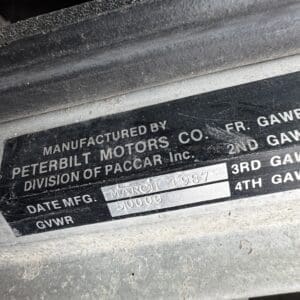 Close-up of a metal vehicle data plate: Manufactured by Peterbilt Motors Co., Division of PACCAR Inc; Date Mfg March 1987; GVWR 50,000 lbs (dusty panel).