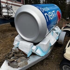 Large Pepsi Next can on a trailer outdoors, with foam insulation blocks and a towing hitch nearby, in a wooded area.