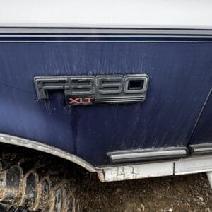 Blue Ford F-350 XLT badge on a dirty blue pickup, with a muddy tire and ground beneath.