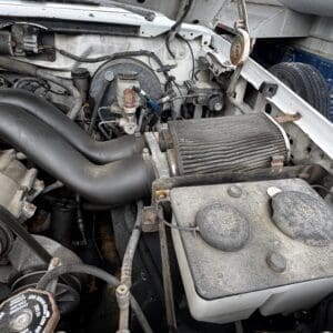 Under-hood view of a dusty engine bay with a large cone air filter and various hoses.