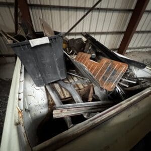 Rusty pickup truck bed filled with scrap metal and assorted debris inside a metal shed.