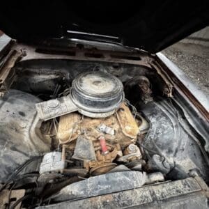 Rusty, dusty car engine under an open hood in an old, neglected engine bay — metal surfaces corroded and covered in grime.