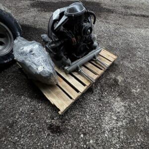 Industrial engine on a wooden pallet outdoors, on a gravel surface, with a plastic-wrapped component beside it.