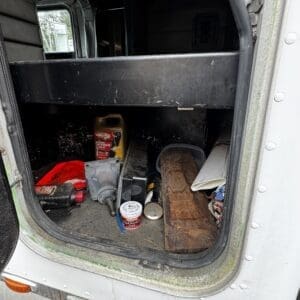 Open truck cargo area with scattered tools and containers: oil jug, cans, wooden plank, red cloth, and papers on the floor.