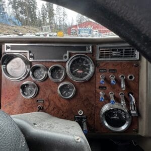 Close-up of a vintage truck dashboard with wood paneling, multiple round gauges, and blue knobs.