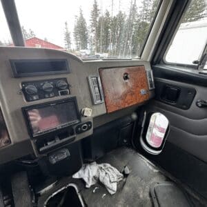 Interior of a truck cab: dusty dashboard, wooden glove-box panel, and debris on the dirty floor with a rag lying around