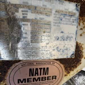 Close-up of a dirty metal trailer ID plate with Featherlite branding and a pink NATM Member sticker visible below.