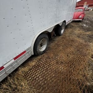 White box trailer with dual wheels on a grassy, muddy lot; a red vintage car and red barn appear in the background.