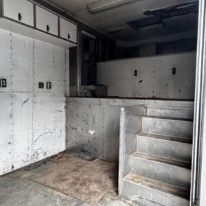 Industrial loading area with white, scratched walls, metal stairs, and a dirty rug on the floor