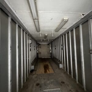 Interior of an empty metal cargo trailer with a wooden plank on the floor and overhead fluorescent lights, extending to the back door.