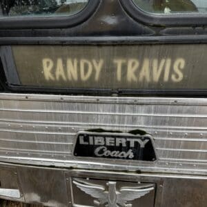 Back of a weathered Liberty Coach bus with 'RANDY TRAVIS' spray-painted on the rear window