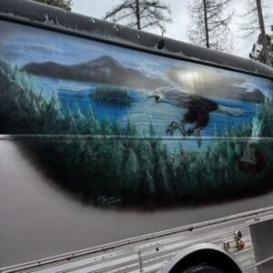 Bus side with a mural of a forest, lake, and mountains, featuring a large bird swooping over the water.