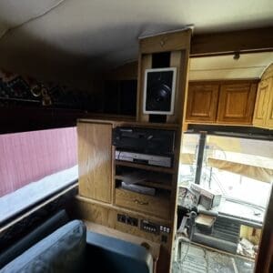 Wooden cabinet wall with stereo equipment and a speaker mounted above, inside a bus or RV cockpit area.