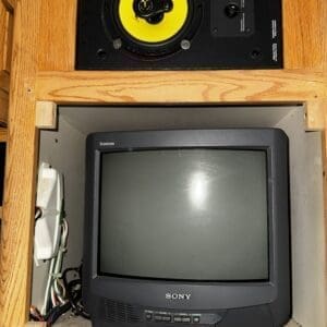 Wooden built-in cabinet with a yellow-speaker unit above and a CRT Sony Trinitron TV below, with wiring along the left side.