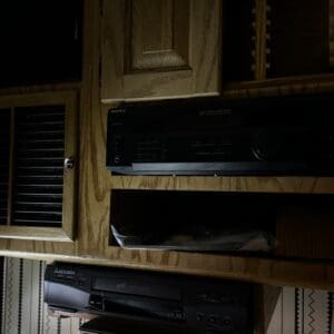 Wooden cabinet with multiple black AV components: a Sony receiver, a DVD/VCR stack below, and shelves around them.