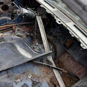 Rusty, abandoned car interior with exposed wiring, missing dashboard panels, and debris scattered on the floor