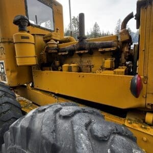 Yellow Caterpillar heavy equipment engine visible with large treaded tire in foreground and dusty exterior detail.