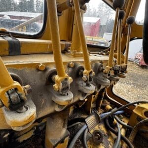 Close-up of yellow construction machine control levers and joints, dusty from use, inside a cab.