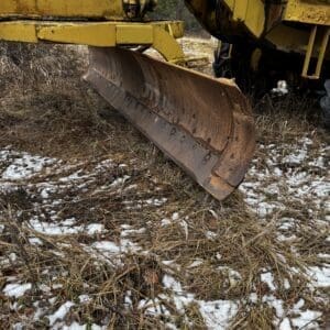 Yellow heavy construction equipment blade in a field with patches of snow and dry grass.