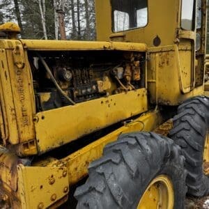 Old yellow tractor with the hood open, exposing the engine, and large rugged tires in a wooded area.