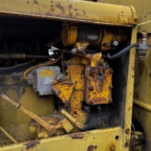 Close-up of a weathered yellow industrial engine with rusted components and hoses showing wear and dirt.