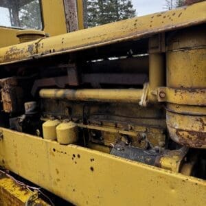 Close-up of a weathered yellow construction machine with exposed engine components and rusted paint.