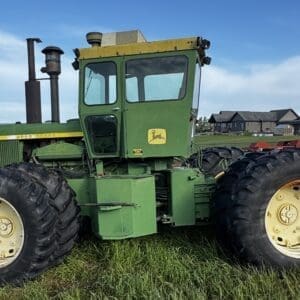 LOT 43 1 - Montana Auctions by Kevin Hill Green John Deere tractor with oversized rear tires parked on a grassy field, with rural houses in the background.