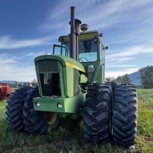 LOT 43 2 - Montana Auctions by Kevin Hill Green John Deere 7520 tractor with dual rear tires parked on a grassy field under a blue sky.